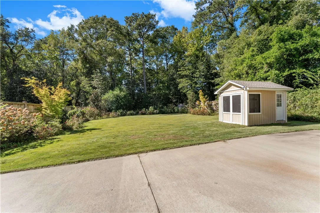 A spacious grassy lawn bordered by mature trees features a detached storage shed.