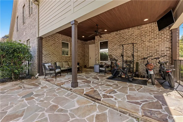 A spacious stone patio sits beneath a covered wood-paneled ceiling alongside brick exterior walls.