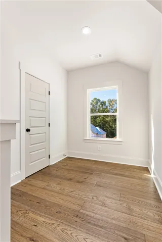 Rich hardwood flooring complements the vaulted ceiling and natural window views in this versatile alcove.