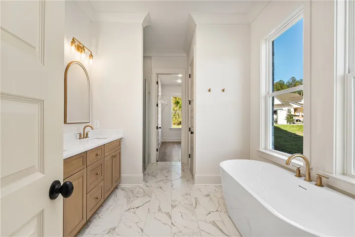 Elegant crown molding, marble-style tile flooring, and a freestanding soaking tub define this bathroom.