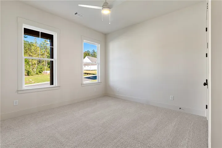 Double windows frame leafy outdoor views, illuminating this clean carpeted bedroom.