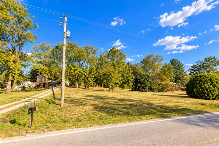 A spacious grassy lot bordered by mature trees sits under a clear blue sky.