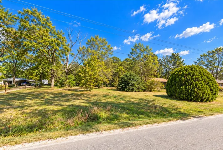 Mature trees frame a sprawling grassy lot under a clear blue sky.