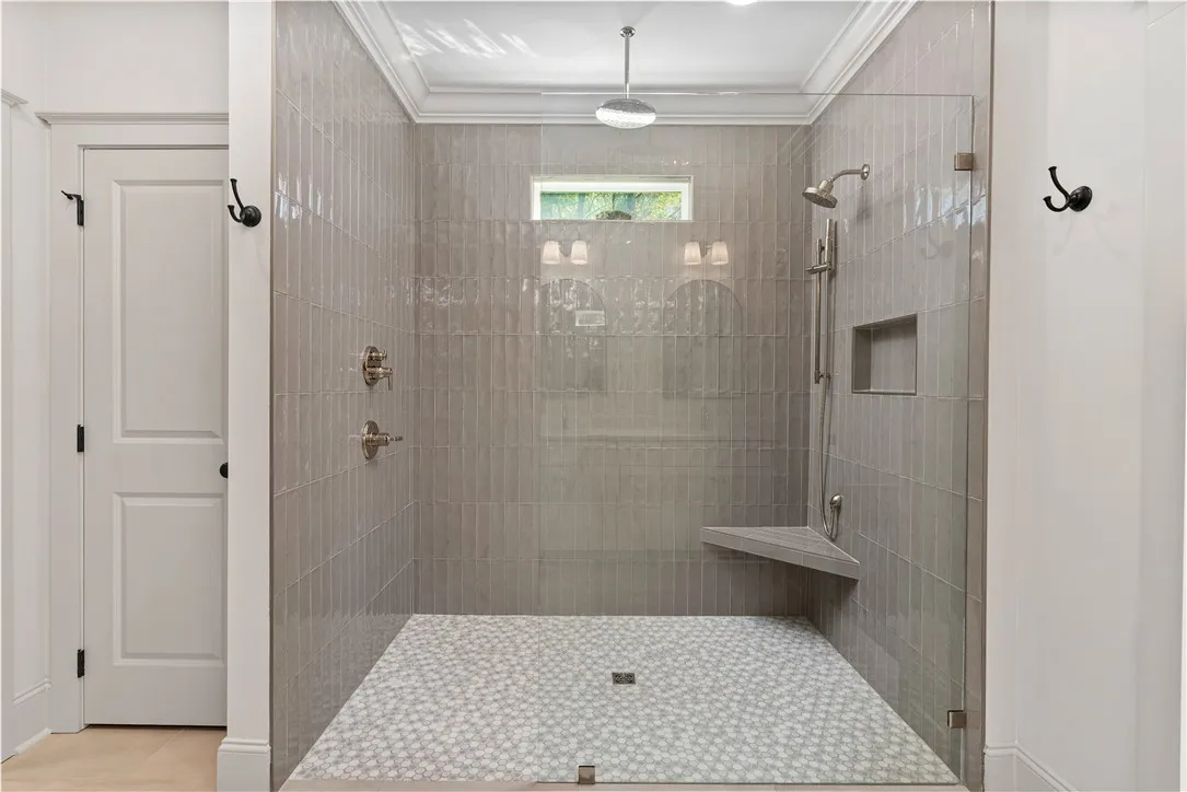 An elegant walk-in shower features vertical wall tiling, patterned floor tile, and sleek glass paneling.