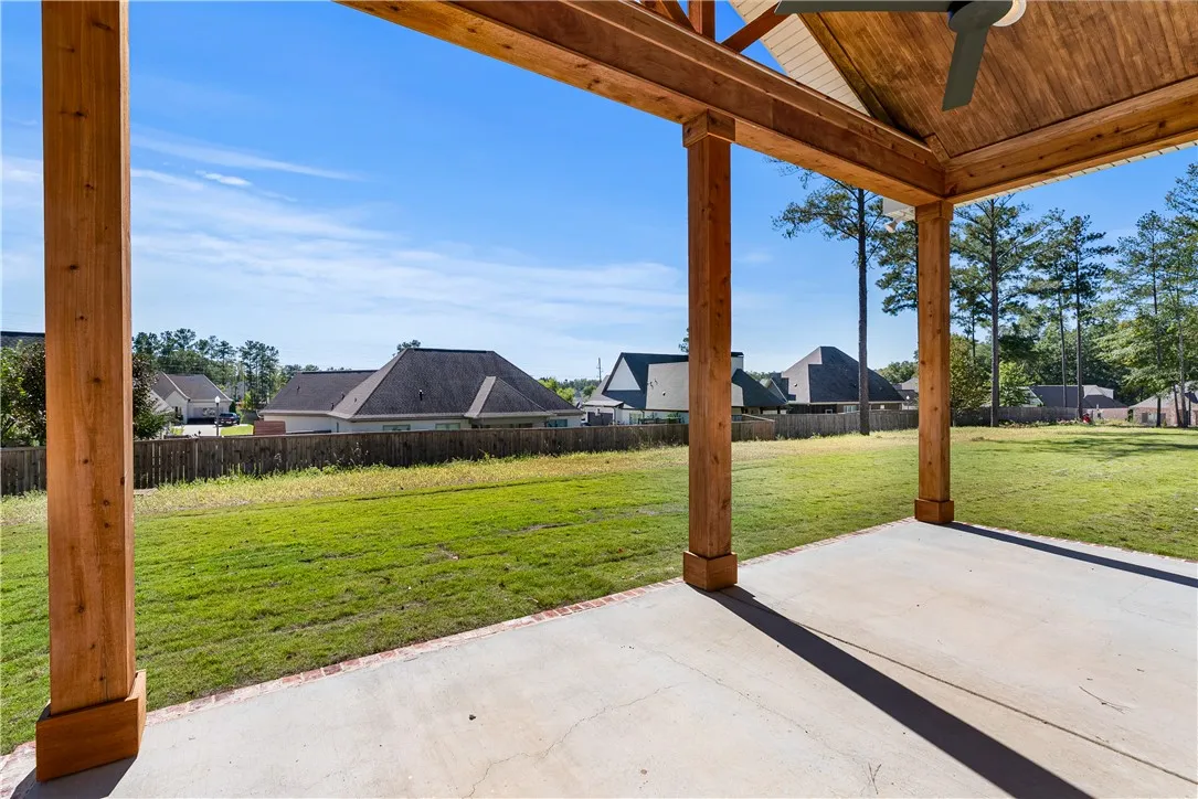 A spacious covered concrete patio framed by heavy timber columns overlooks a grassy fenced yard.