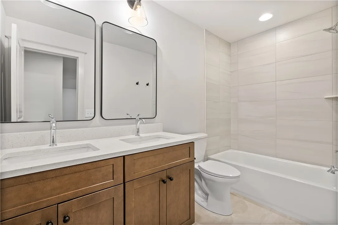 A refined bathroom features a dual vanity, sleek tile tub surround, and warm wood cabinetry.