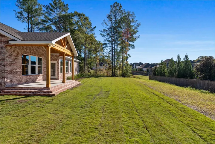 A spacious grassy yard stretches alongside a brick exterior featuring a covered back porch.