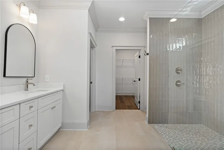 Crown molding accents this modern washroom featuring a tiled walk-in shower and stone countertops.