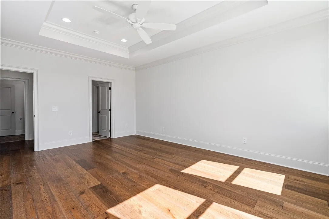 Rich hardwood flooring complements the elegant tray ceiling details in this spacious master bedroom.