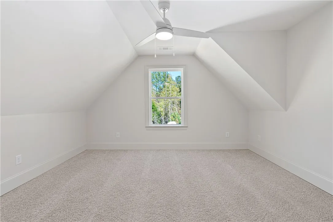 Slanted ceilings frame a cozy upper-level space featuring plush carpeting and a woodland view.