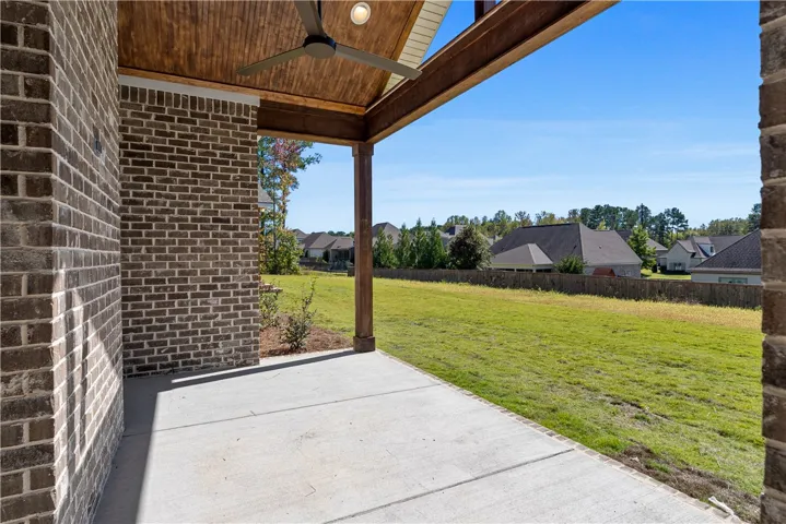 An inviting covered patio features a warm wood ceiling and overlooks a sprawling grassy lawn.