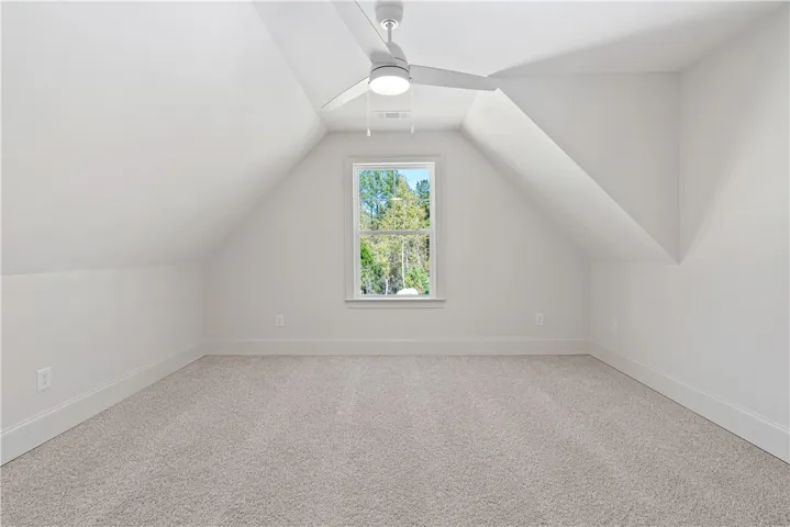Slanted ceilings frame a cozy upper-level space featuring plush carpeting and a woodland view.
