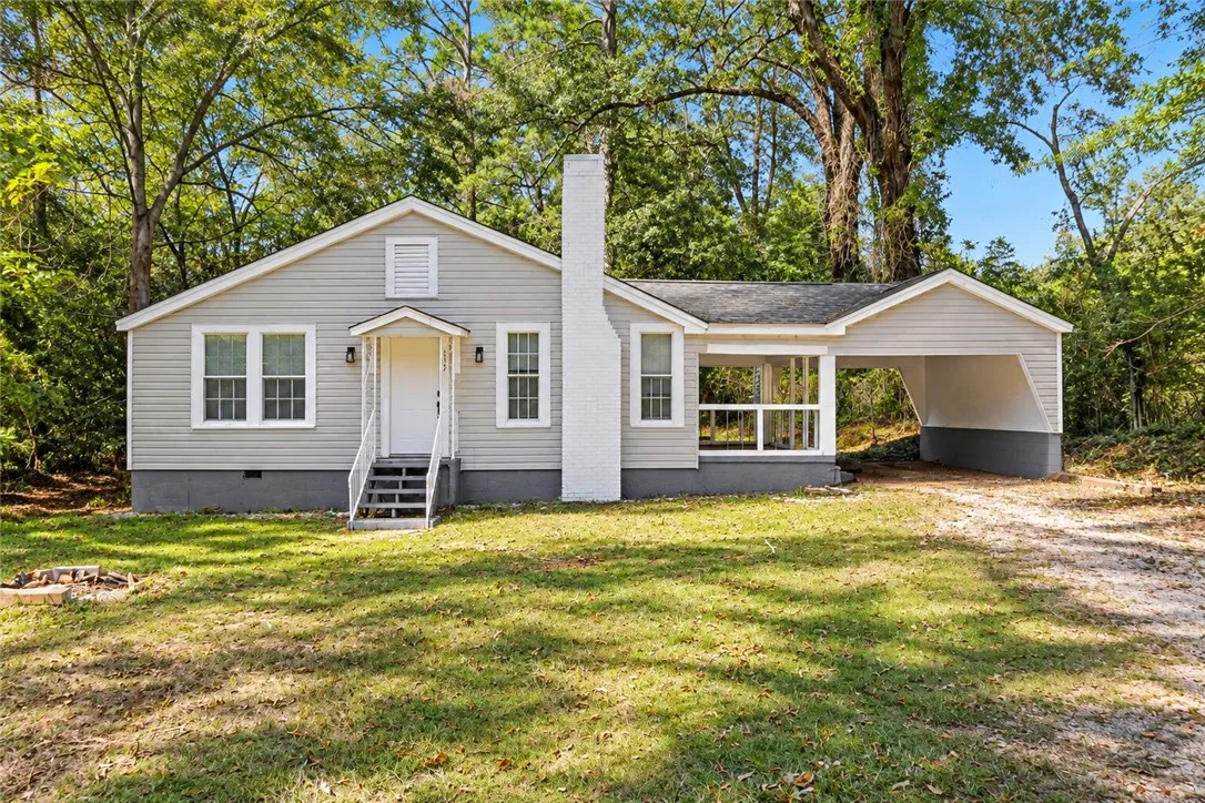 A classic ranch exterior showcases light-colored siding, a prominent brick chimney, and an attached carport.