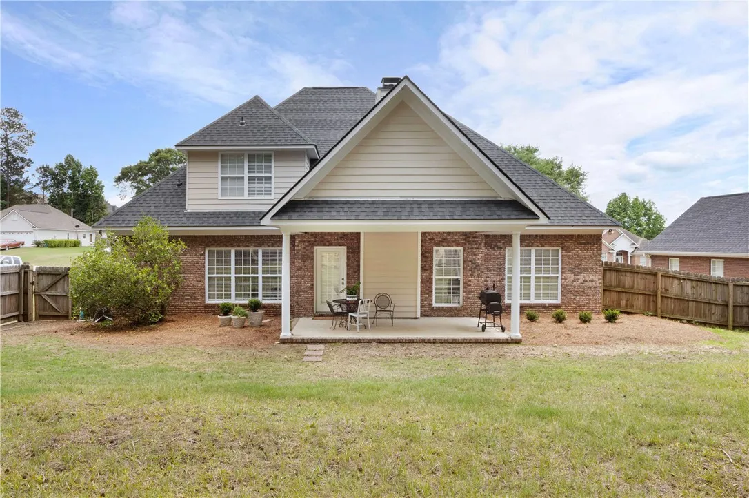 A covered back patio overlooks the grassy yard enclosed by wooden fencing.