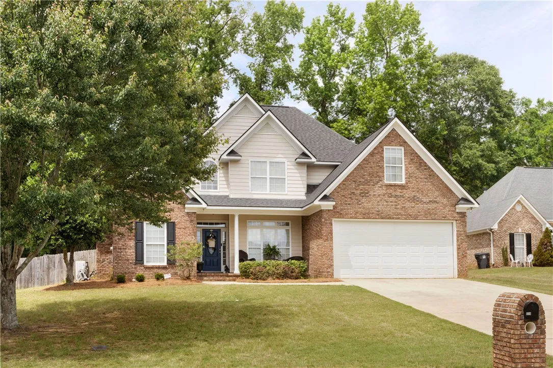 Mature trees frame a classic brick and siding facade with an attached two-car garage.