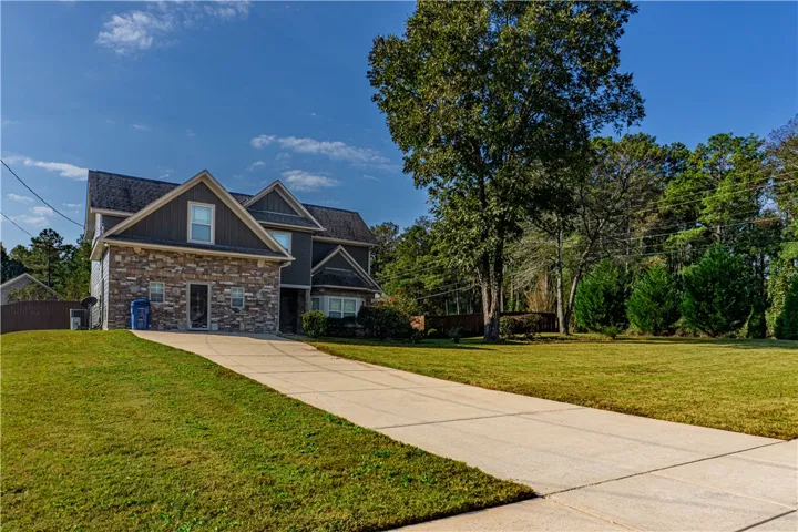 A long concrete driveway sweeps up to a multi-level home featuring prominent stone veneer accents.