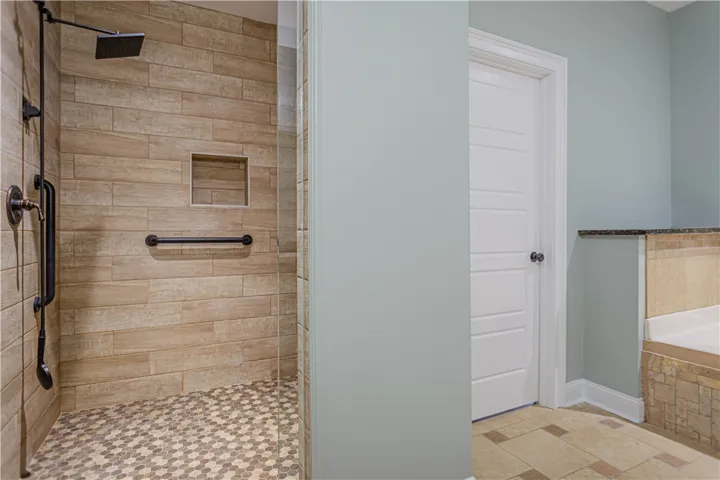 A walk-in tile shower stands alongside a separate soaking tub and neutral tile flooring.