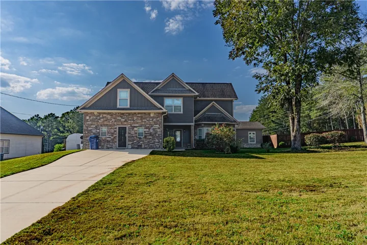 A spacious concrete driveway leads toward this multi-level home featuring stone veneer accents.