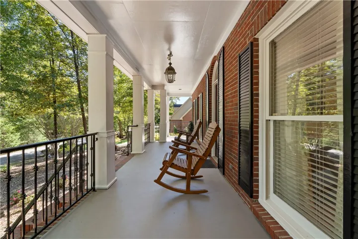 A spacious covered front porch features classic columns, wrought iron railings, and brick accents.