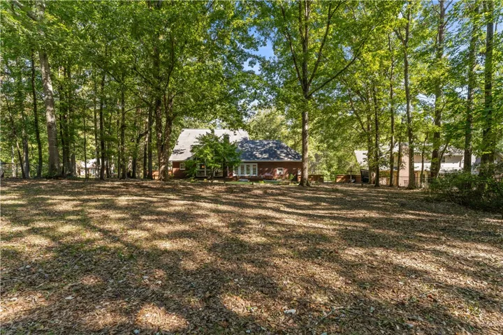 Mature trees frame a spacious, shaded backyard overlooking the rear exterior of the home.