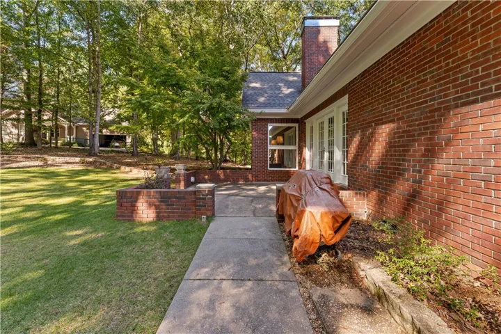A spacious concrete patio stretches alongside classic red brick walls bordering a grassy lawn.