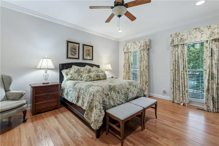 Warm hardwood floors and classic crown molding elevate this serene and comfortable bedroom setting.