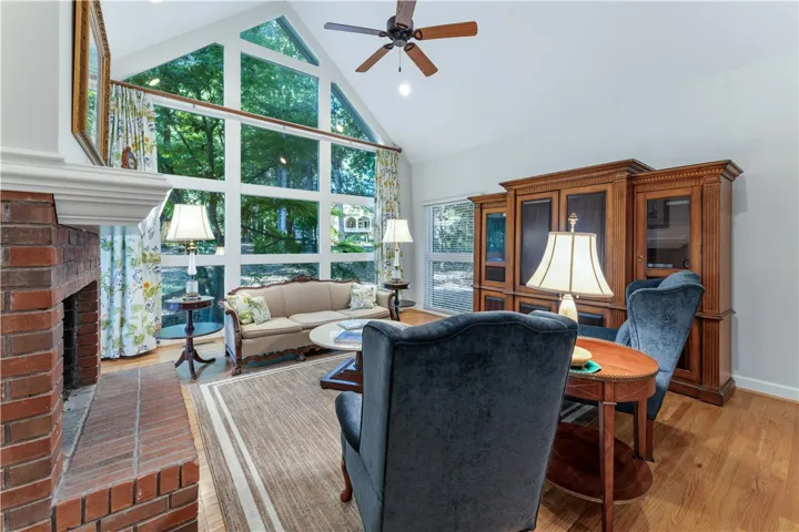 Floor-to-ceiling windows frame serene wooded views alongside a classic brick fireplace.