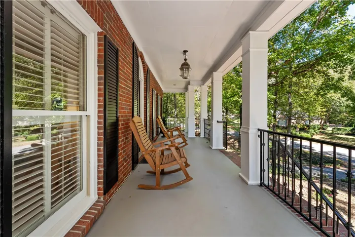 An inviting covered front porch showcases classic brick siding, stately columns, and decorative metal railings.