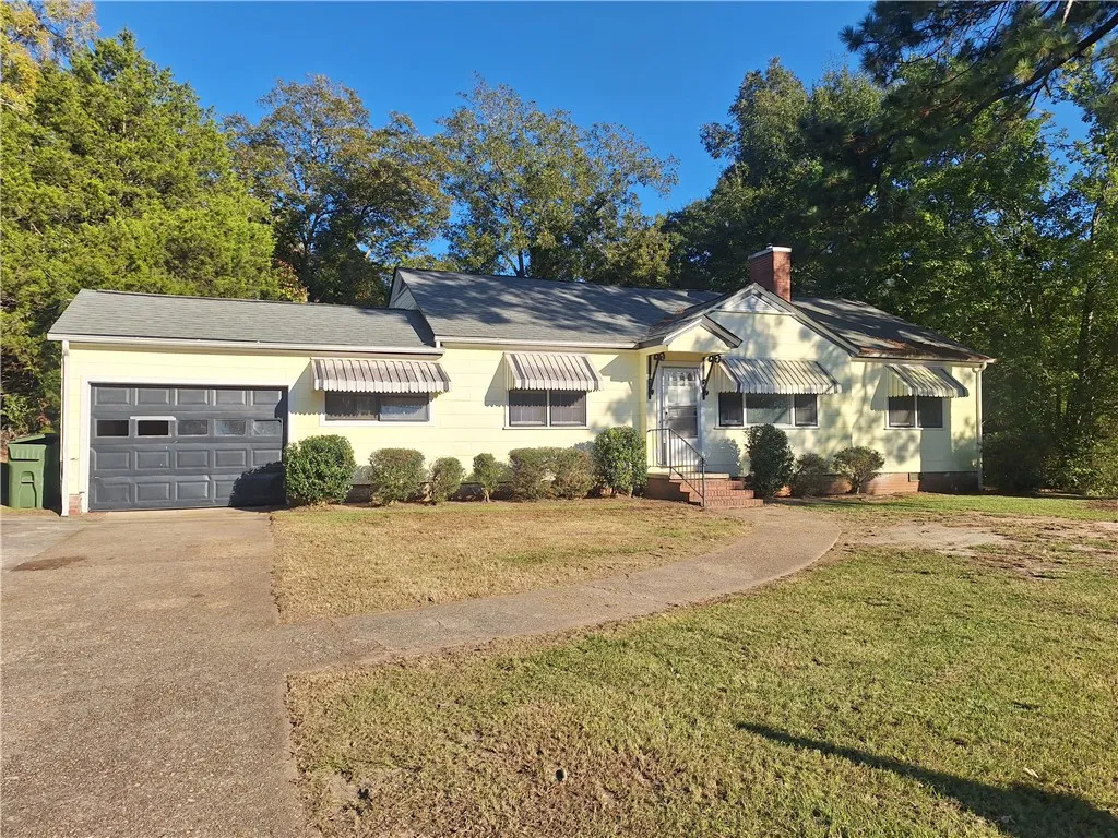 A classic ranch exterior with a level lawn, mature trees, and attached garage.