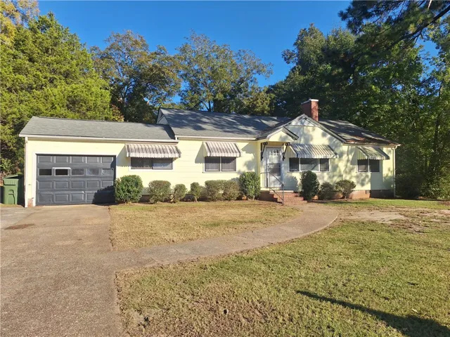 A classic ranch exterior with a level lawn, mature trees, and attached garage.