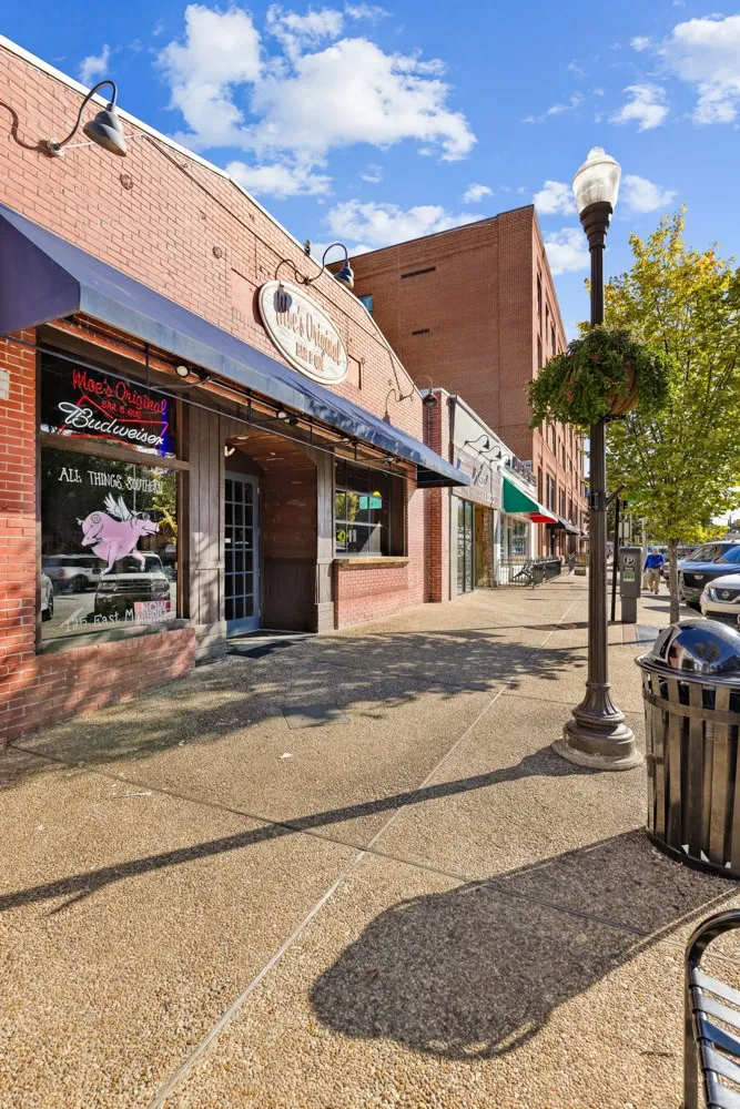 Classic brick storefronts line a wide paved sidewalk under blue skies.