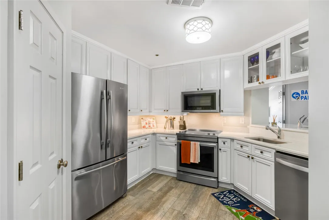 White cabinetry and stainless steel appliances pair with warm wood-inspired flooring.
