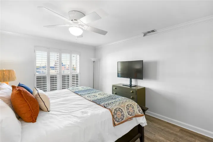 Crown molding frames the bedroom, which includes wood flooring and custom plantation shutters.