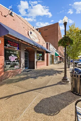 Classic brick storefronts line a wide paved sidewalk under blue skies.