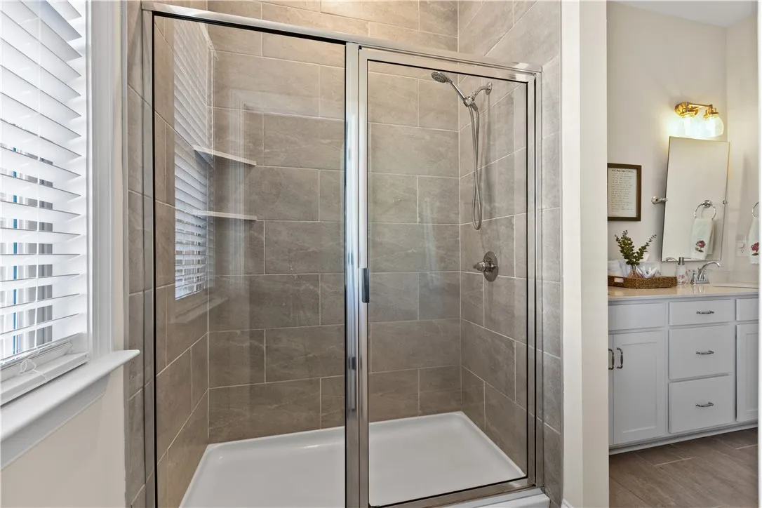 Floor-to-ceiling tile surrounds a modern glass-enclosed shower across from  the private water closet.