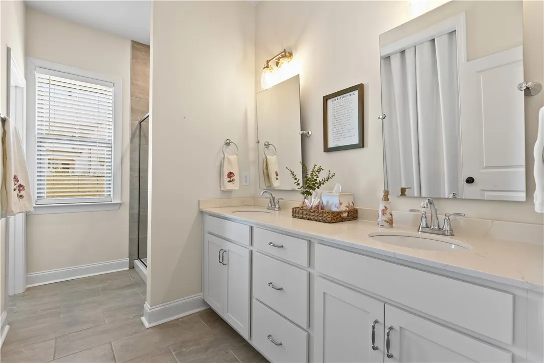Clean lines and stone counters define this ensuite bathroom with a dual vanity and tile flooring.