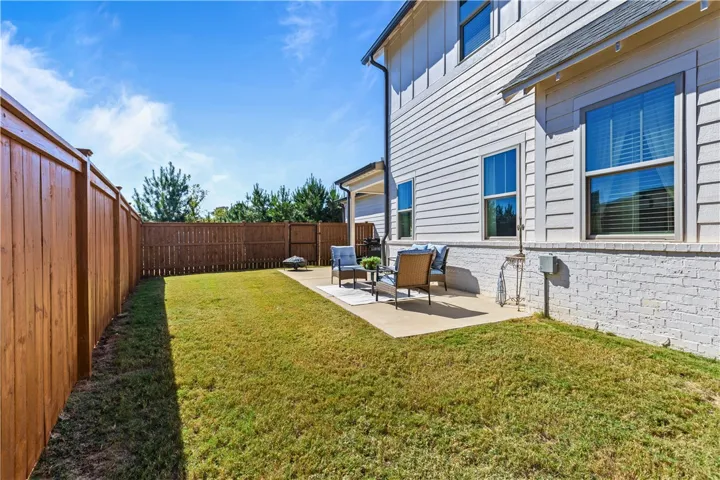 An inviting concrete patio overlooks a grassy, fully fenced backyard under clear blue skies.