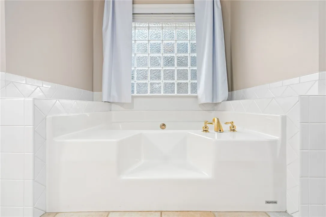 Classical tiling surrounds a deep soaking tub positioned below a glass block privacy window.