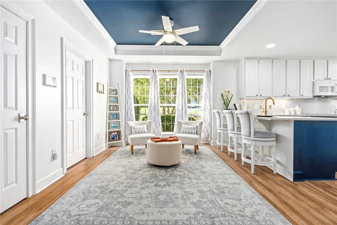 An open living and dining area features polished wood flooring under a deep blue tray ceiling.
