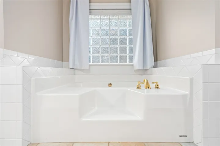 Classical tiling surrounds a deep soaking tub positioned below a glass block privacy window.