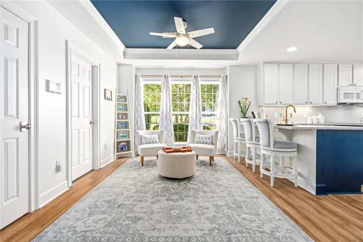 An open living and dining area features polished wood flooring under a deep blue tray ceiling.