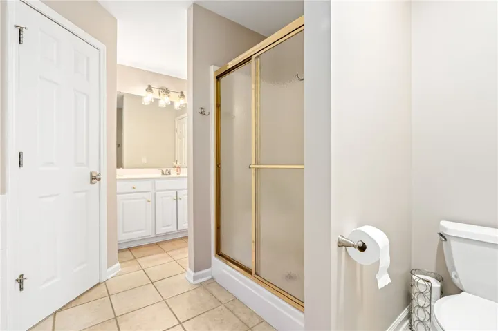 A well-maintained bathroom featuring a walk-in shower with gold-trimmed sliding glass doors and neutral tile flooring.