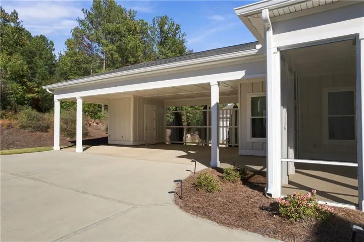 An expansive covered carport connects seamlessly to a concrete driveway and adjacent screened porch.