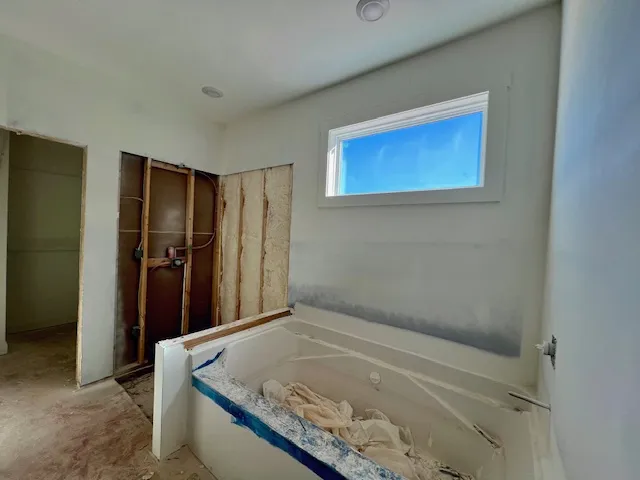 Unfinished bathroom featuring a large soaking tub, recessed lighting, and a high-set transom window.