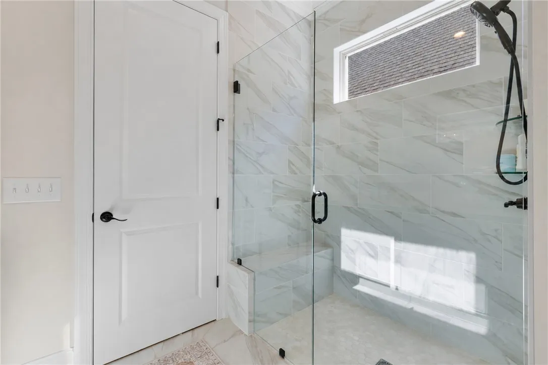 A glass-enclosed walk-in shower showcases elegant marble-patterned tile walls and a built-in bench.