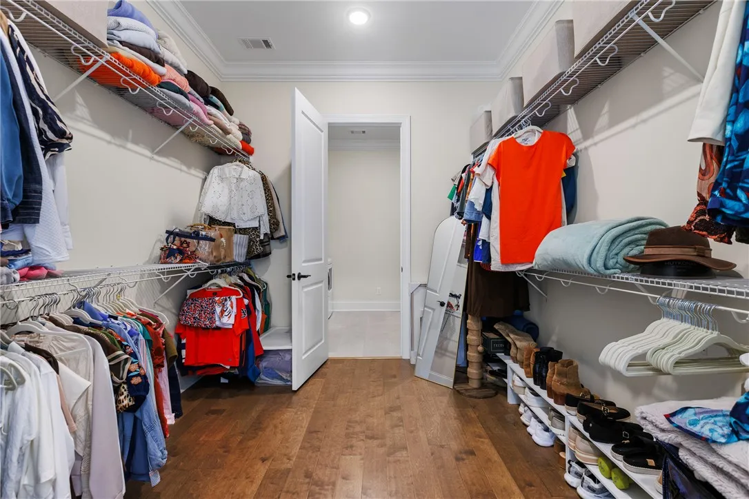 A spacious closet features rich wood flooring, detailed crown molding, and extensive built-in wire shelving.