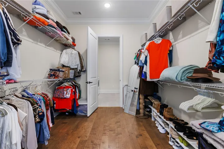 A spacious closet features rich wood flooring, detailed crown molding, and extensive built-in wire shelving.