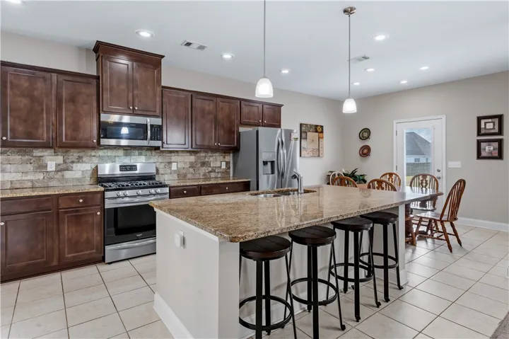 Rich wood cabinetry and a central granite island anchor this functional tile-floored kitchen.