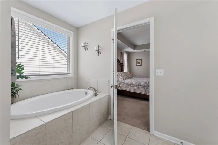 An inviting soaking tub positioned beneath a large window offers views directly into the bedroom.