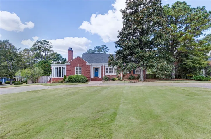 Stately brick exterior anchors a sprawling green lawn beneath mature shade trees.